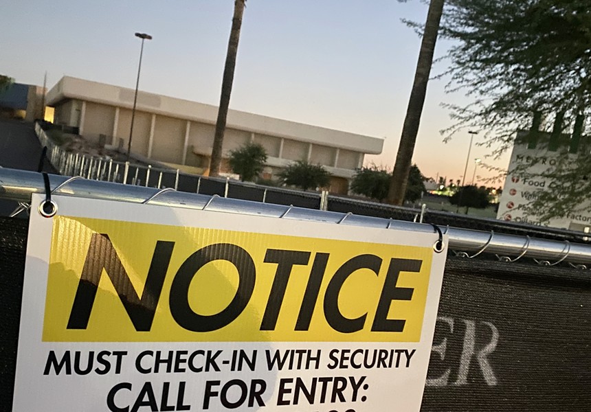 A sign on a fence in front of a defunct mall.