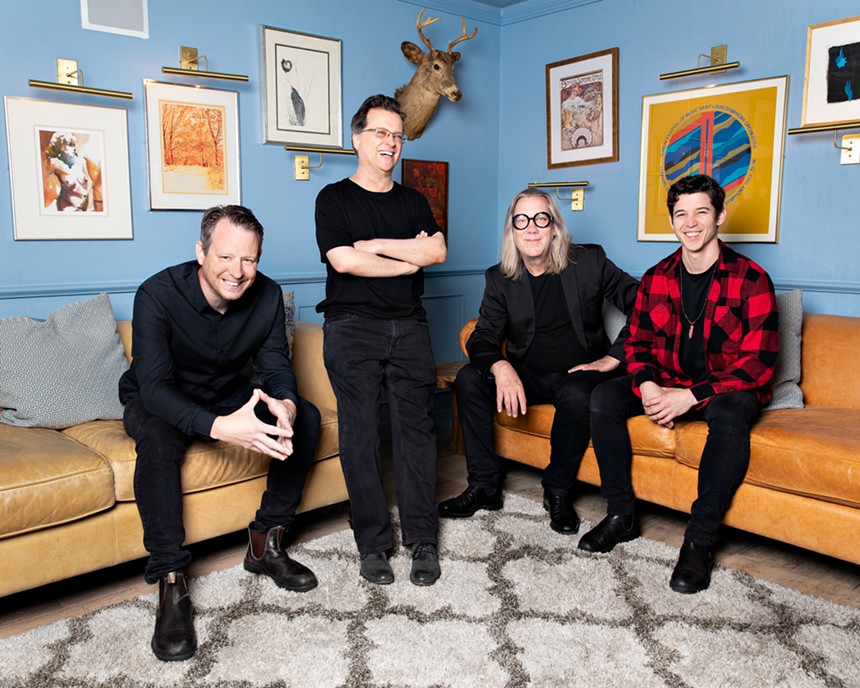 Four members of a rock band standing and sitting in a room.