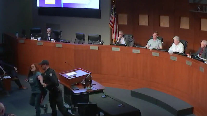 a woman is arrested at a city council meeting