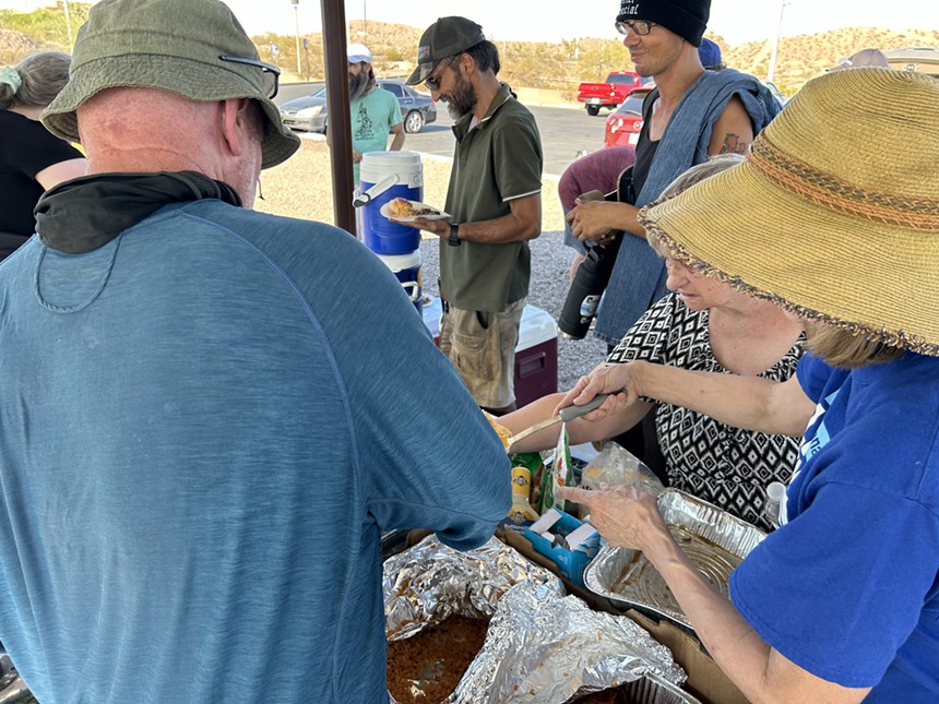 people crowd around food on a picnic table