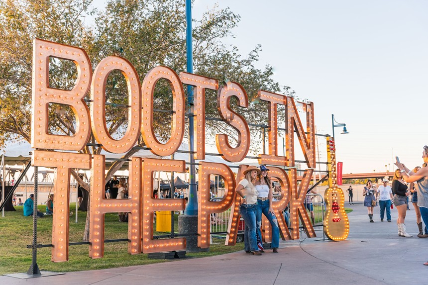 Two women in cowboy hats stand in front of a sign that says "Boots in the Park."