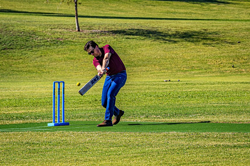 a man in jeans and a maroon shirt swings a cricket bat