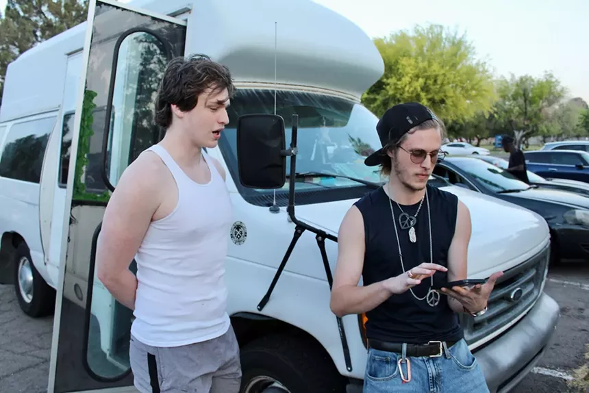 Two men in tank tops leaning on a van.
