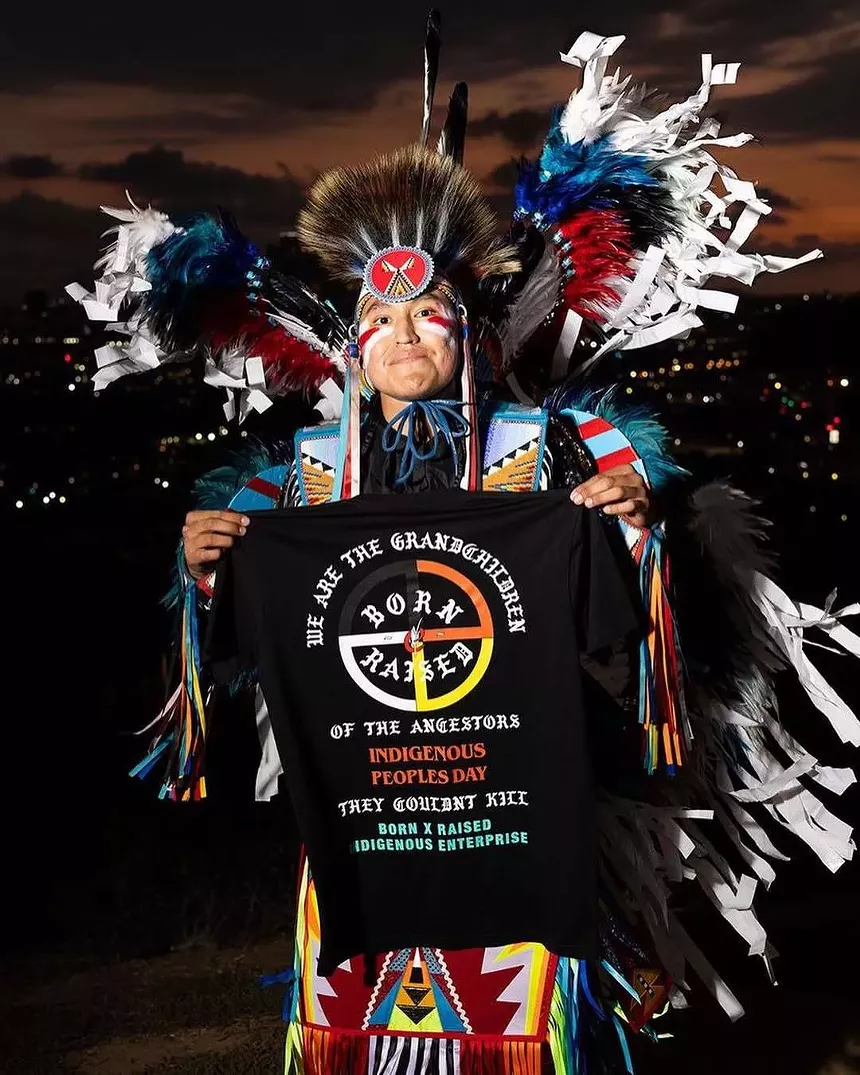 An Indigenous dancer holding up a shirt.