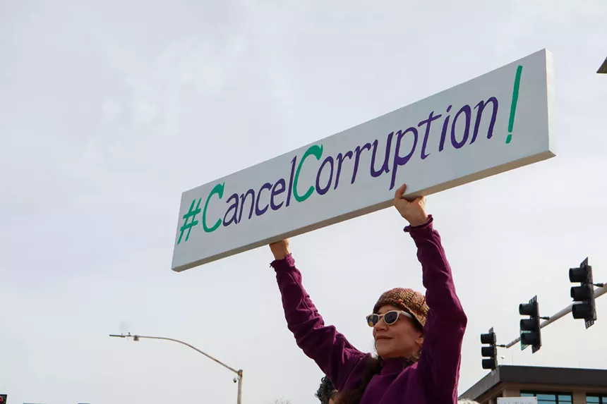 A protester stands with a sign reading “Cancel Corruption."