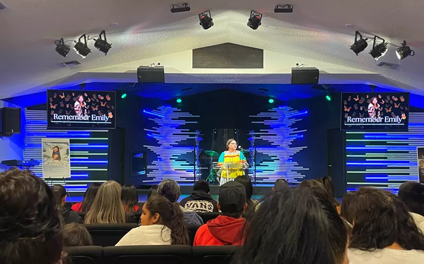 a woman speaks on stage at a church in front of a packed crowd