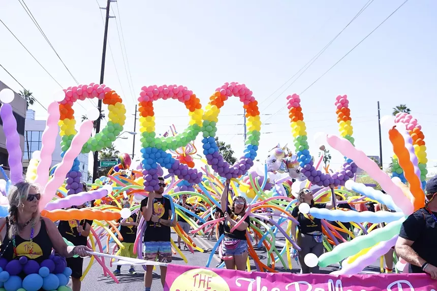 people at a pride parade holding balloons that spell "proud"