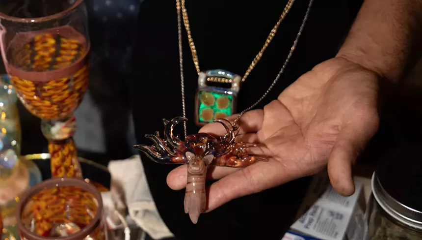 a man's hands show off a glass-blown scorpion on a chain