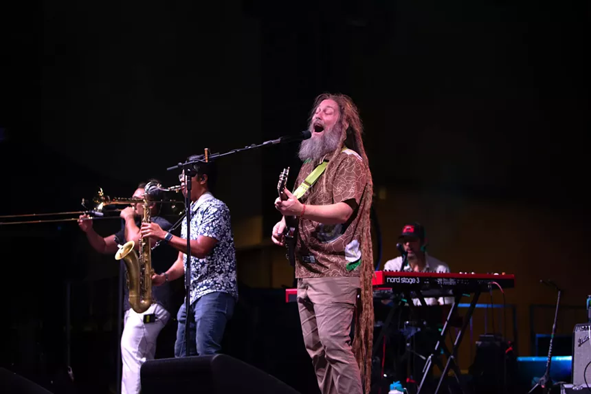 musicians on stage. one plays guitar and sings, one plays saxophone, one plays trombone