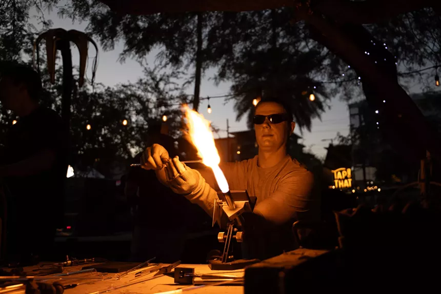 a man in sunglasses rolls molten glass under a torch