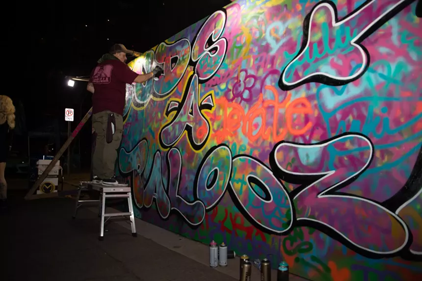 A man spraypaints on a wall that says "buds-a-palooza"