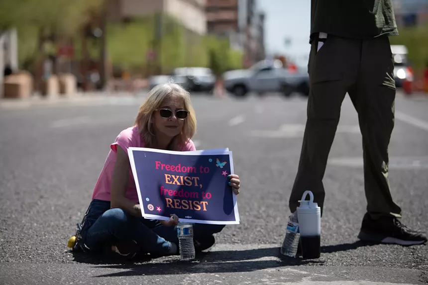 a protester sits in a street with a sign that says "freedom to exist, freedom to resist"
