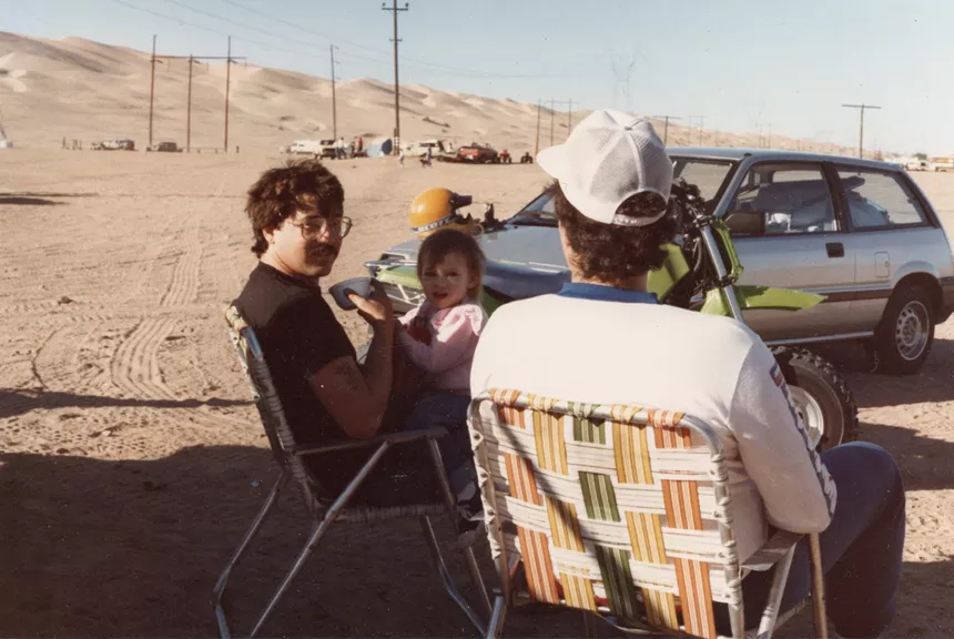 a man sits in a camp chair with a small child in an old photo
