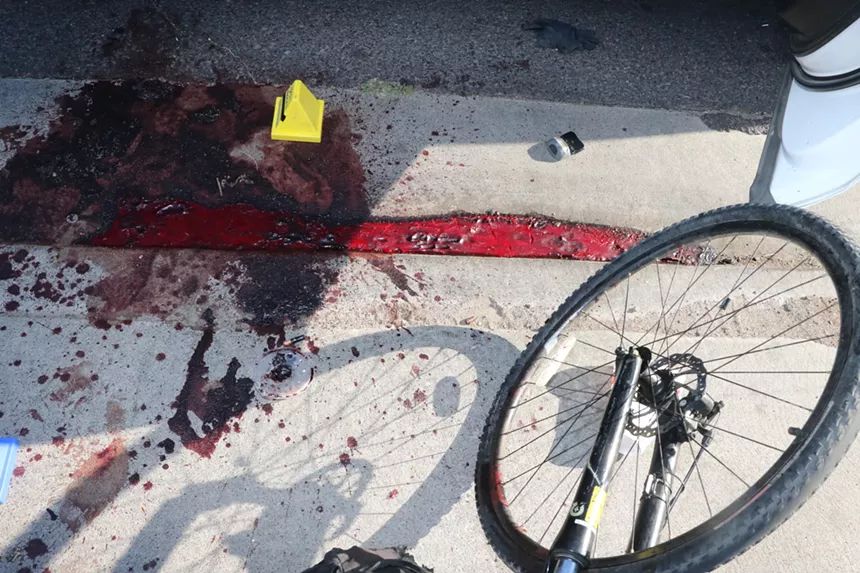 a bike wheel sits next to a pool of blood by a curb
