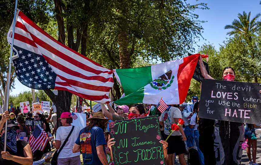 protesters hold aloft an upside-down american flag next to a mexican flag