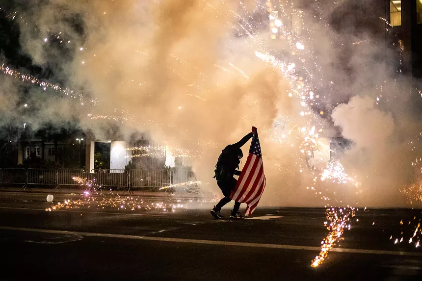A protester uses an American flag to shield himself from tear gas used by Phoenix police to disband a Black Lives Matter protest downtown in May 2020.