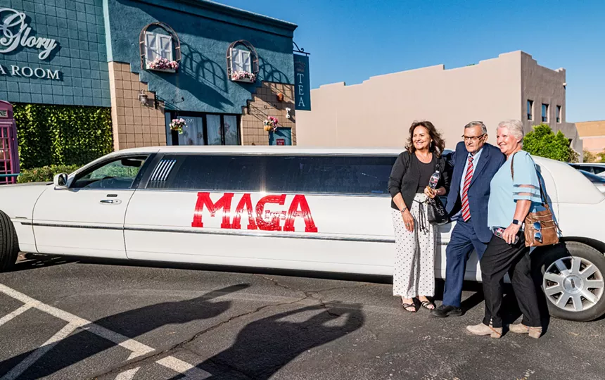 Joe Arpaio and two women pose in front of a white limo that says "MAGA" in red letters.