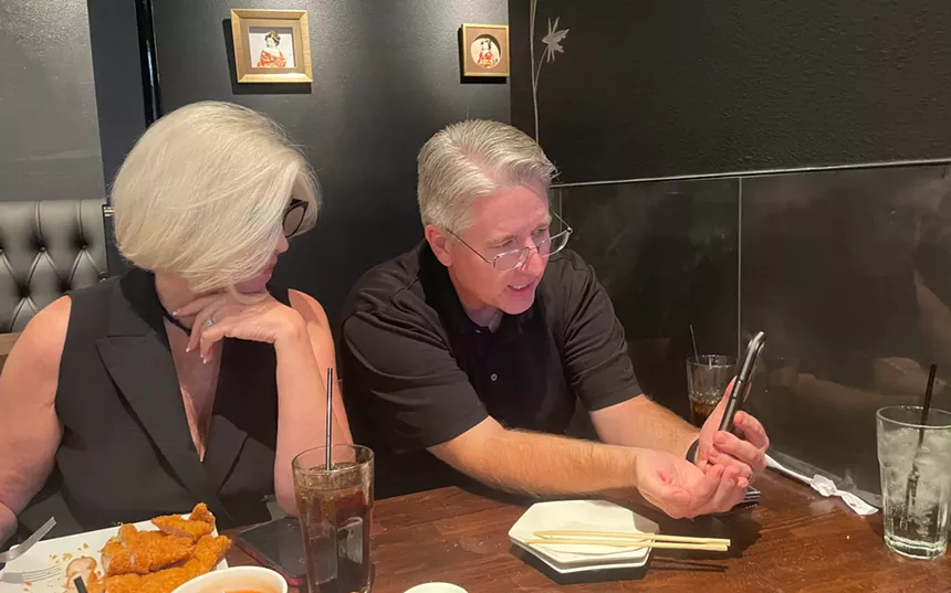 a gray-haired man and woman talk to someone via video chat in a restaurant