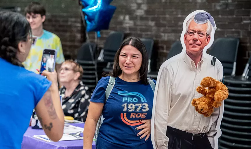 a woman poses with a life-size cardboard cutout of Schweikert, replete with sleeping cap and stuffed toy