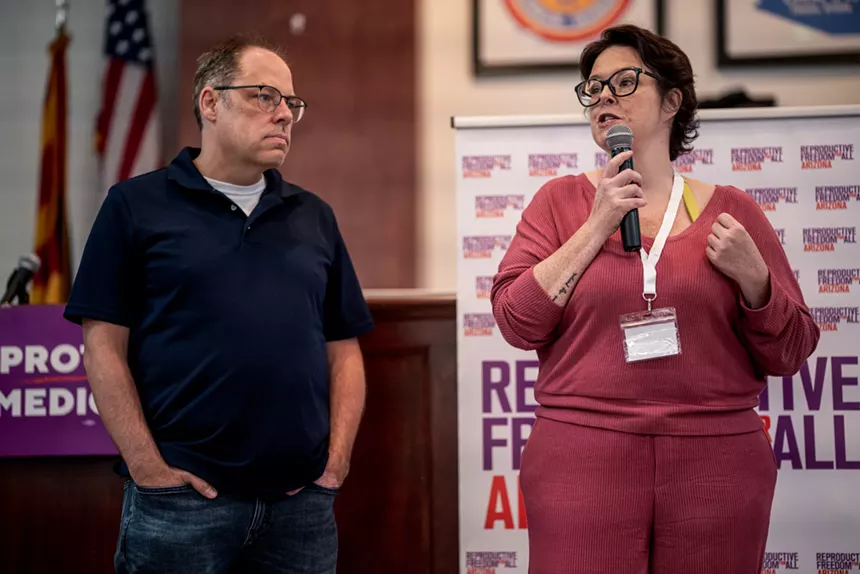 a man and woman stand and speak into a microphone