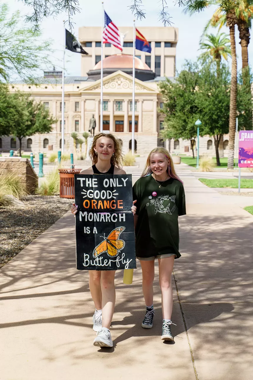 two people pose with a sign that says "the only good orange monarch is a butterfly"