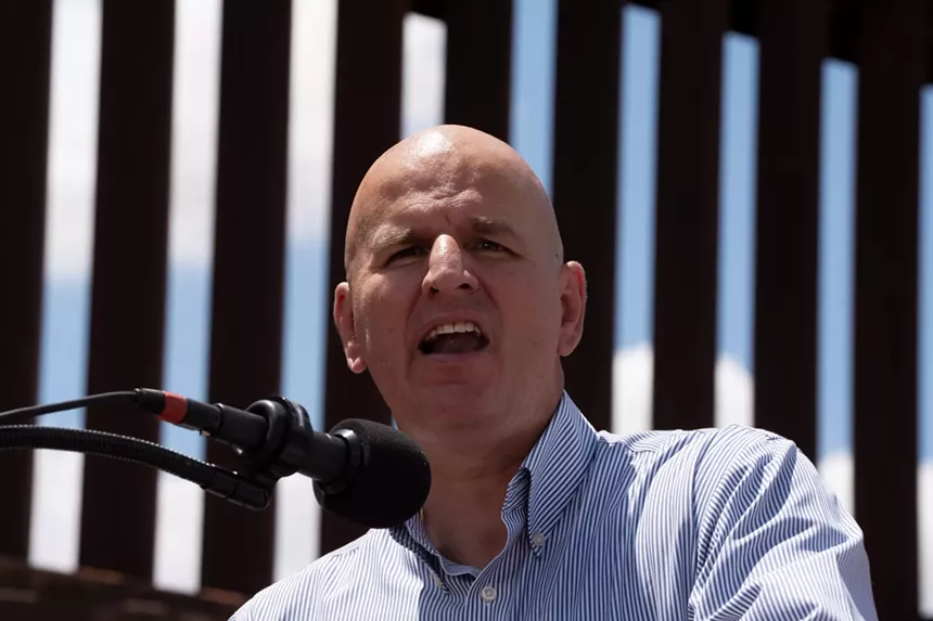 brandon judd speaks into a microphone in front of a border wall
