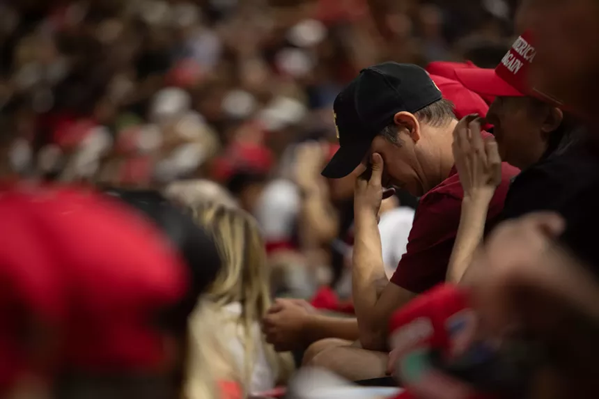 a man in a crowd covers his eyes with his hand as he bends forward in his seat