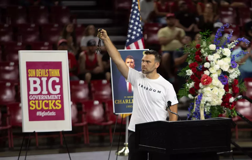 a man in a white "Freedom" shirt holds up a rosary