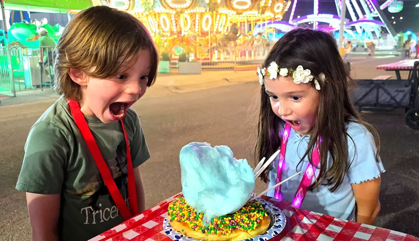 two small children gawk at a huge donut covered in nerds candy and cotton candy
