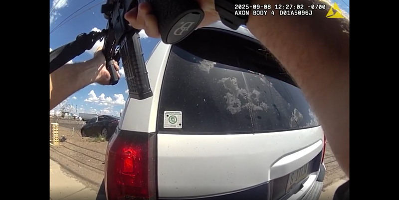 Image: body-camera footage of a person pointing a rifle at a black sedan