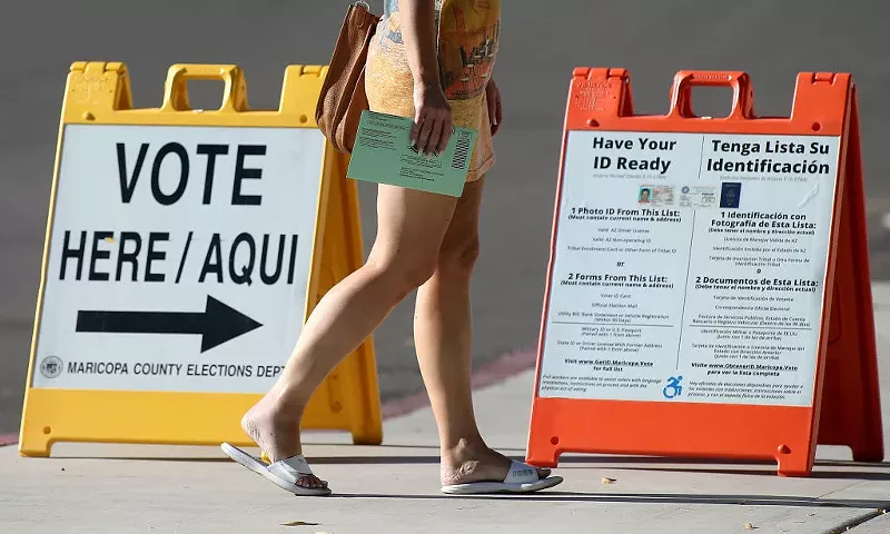 Image: a person walks by a "VOTE" placard with a ballot