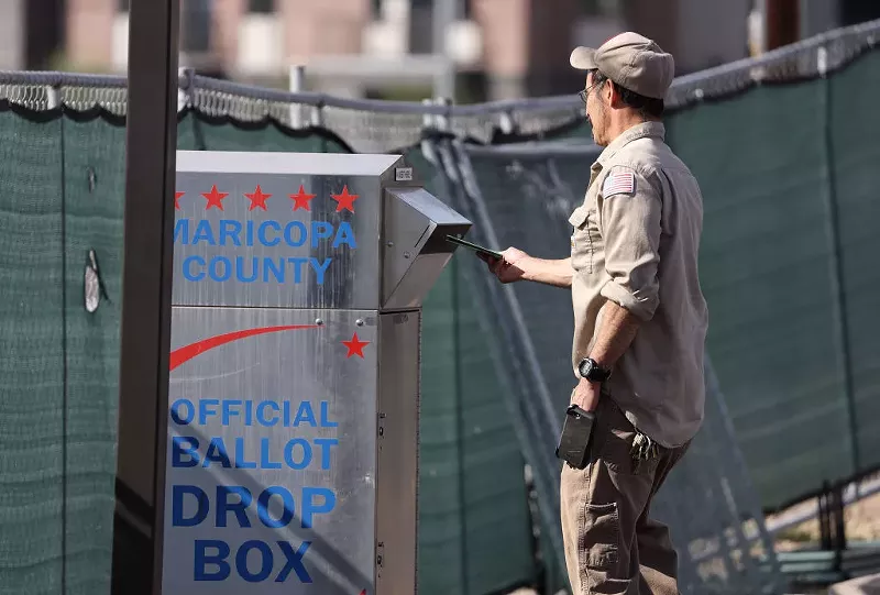 Image: A voter drops his ballot into a drop box at the Maricopa County Tabulation and Election Center