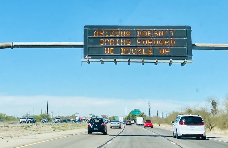 a highway sign that says "Arizona doesn't spring forward, we buckle up"