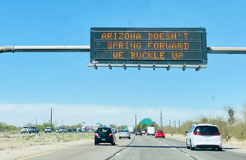 Image: a highway sign that says "Arizona doesn't spring forward, we buckle up"