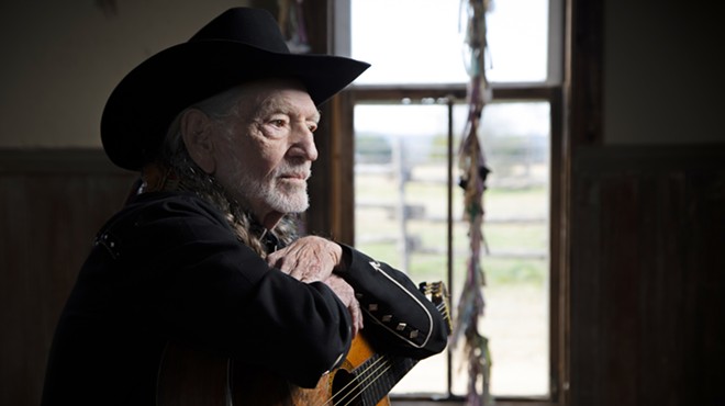 Willie Nelson sits in a room holding a guitar.