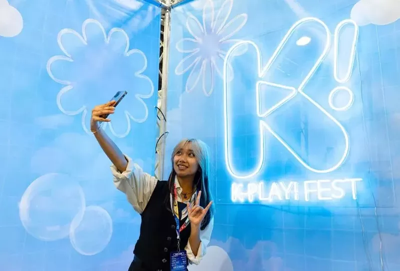 Image: A young woman taking a selfie in front of a blue screen.